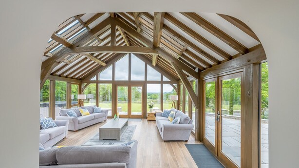 A spacious conservatory with a high ceiling and large windows, furnished with sofas and a coffee table.