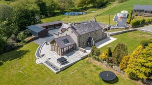 A large, stone house with a spacious patio, a swimming pool, and a well-maintained lawn.
