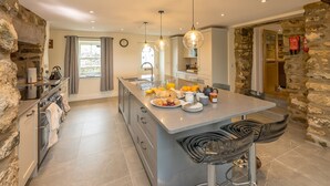 A spacious kitchen with a central island, stone walls, and modern pendant lighting.