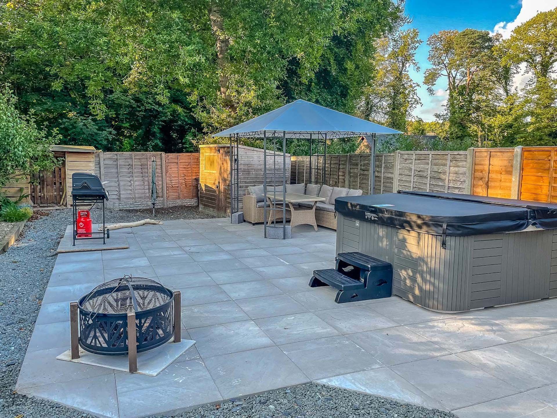 A backyard with a barbecue grill, a hot tub, and a covered seating area.