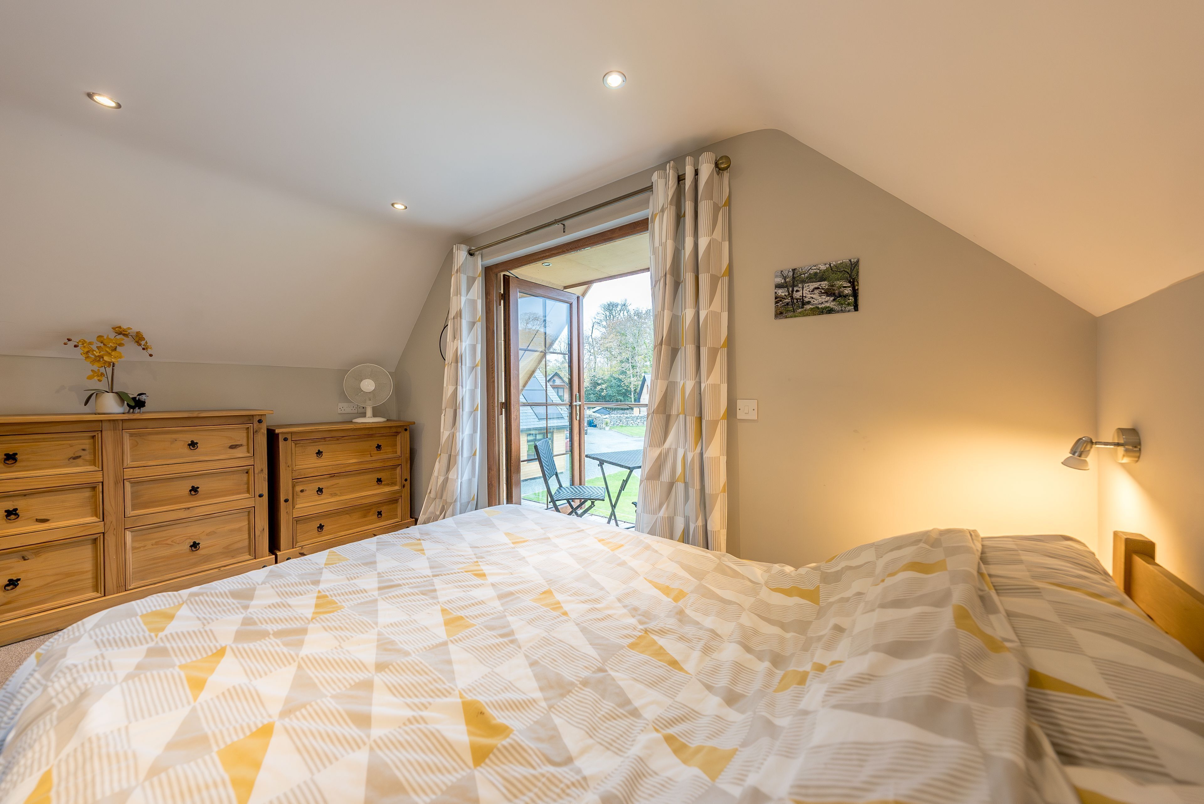 A bedroom with a large bed, wooden dresser, and a view of the outdoors through a window.