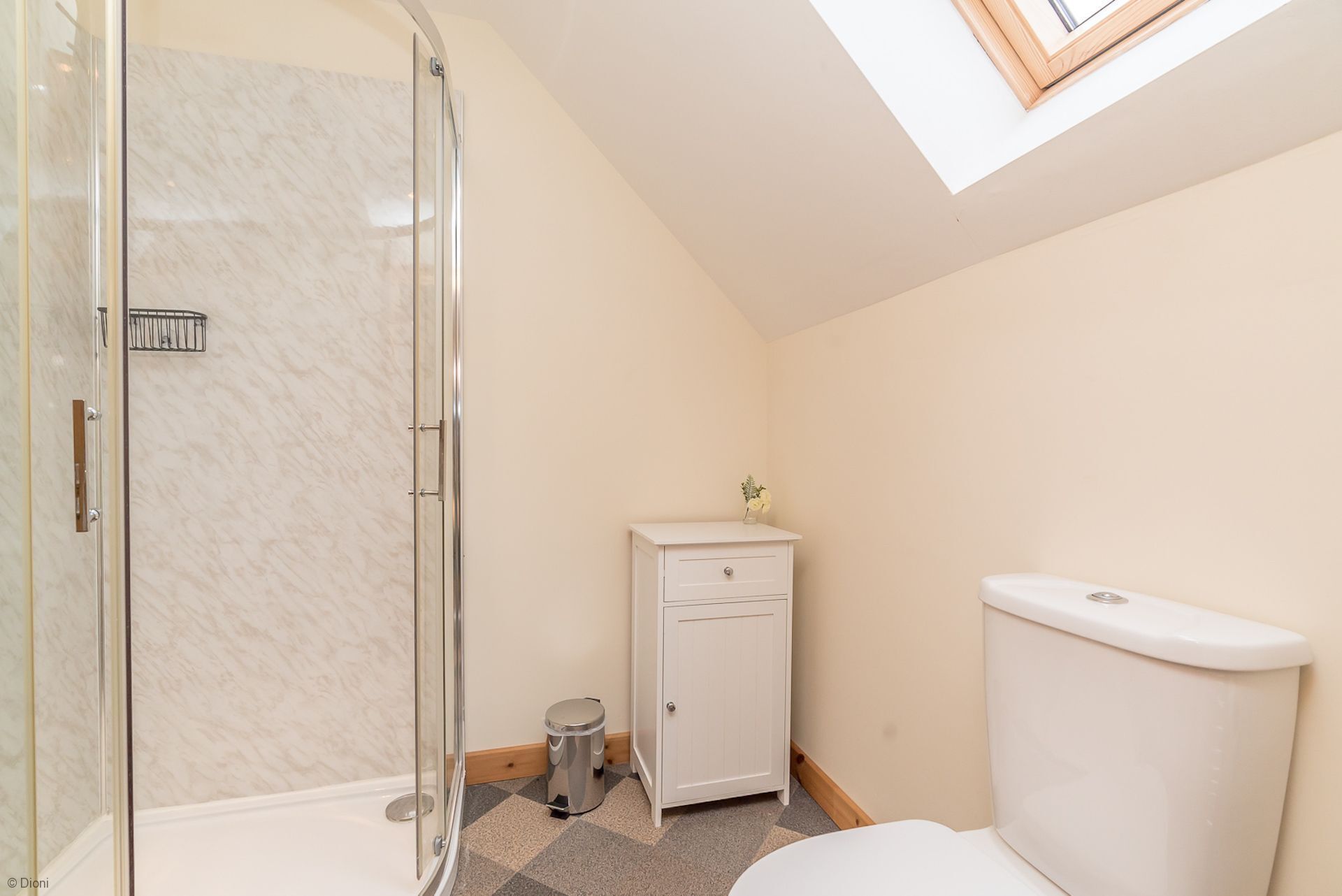 Une salle de bain avec une douche à parois de verre, des toilettes blanches et un petit meuble avec un lavabo.
