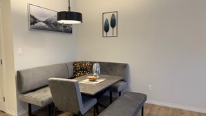 A modern dining area with a gray sofa, bench, and table, featuring a pendant light and framed artwork.