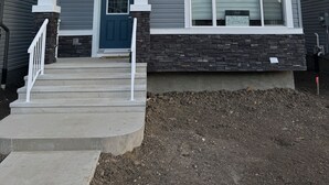 A two-story house with a front porch, a blue door, and a stone foundation.