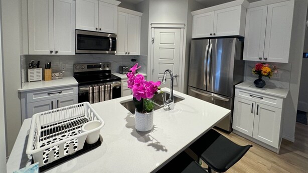 A modern kitchen with white cabinets, stainless steel appliances, and a central island with a sink and a vase of flowers.