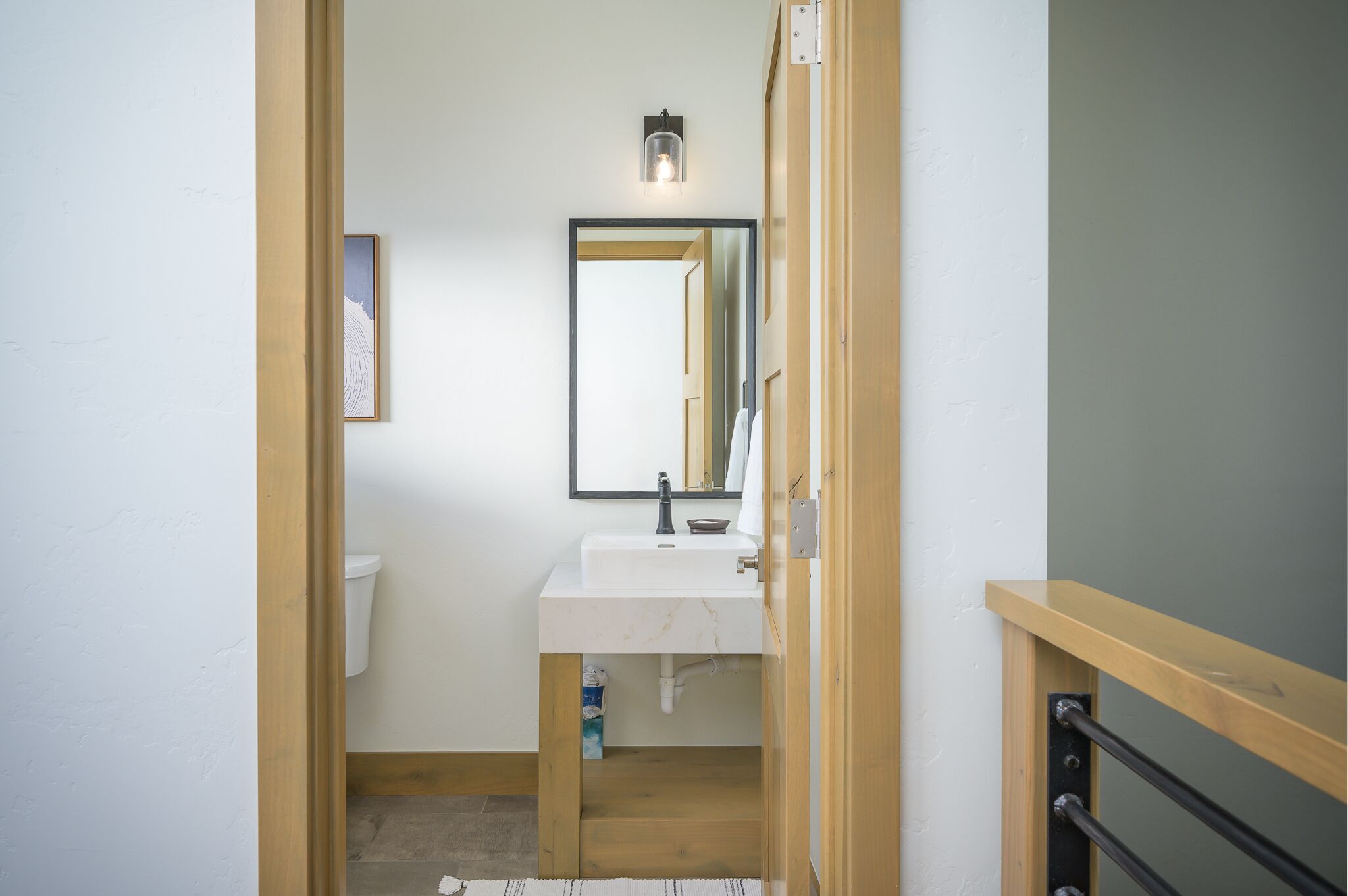 Un baño con un lavamanos blanco, un espejo y una lámpara sobre el espejo.