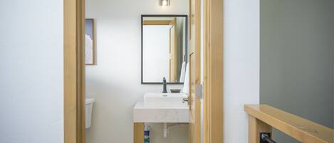 Un baño con un lavamanos blanco, un espejo y una lámpara sobre el espejo.