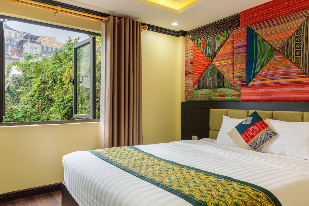 Ein Hotelzimmer mit einem großen Bett, Blick auf Grünfläche und einer farbenfrohen Wandweberei.