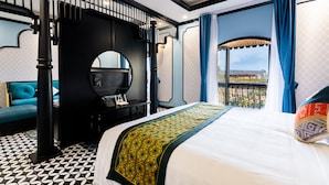 Une chambre d’hôtel avec un grand lit, un sol à motifs noir et blanc, un balcon avec des rideaux bleus et une vue sur l’extérieur.