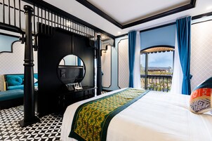 Habitación de hotel con una cama grande, piso con estampado en blanco y negro, balcón con cortinas azules y vistas al exterior.