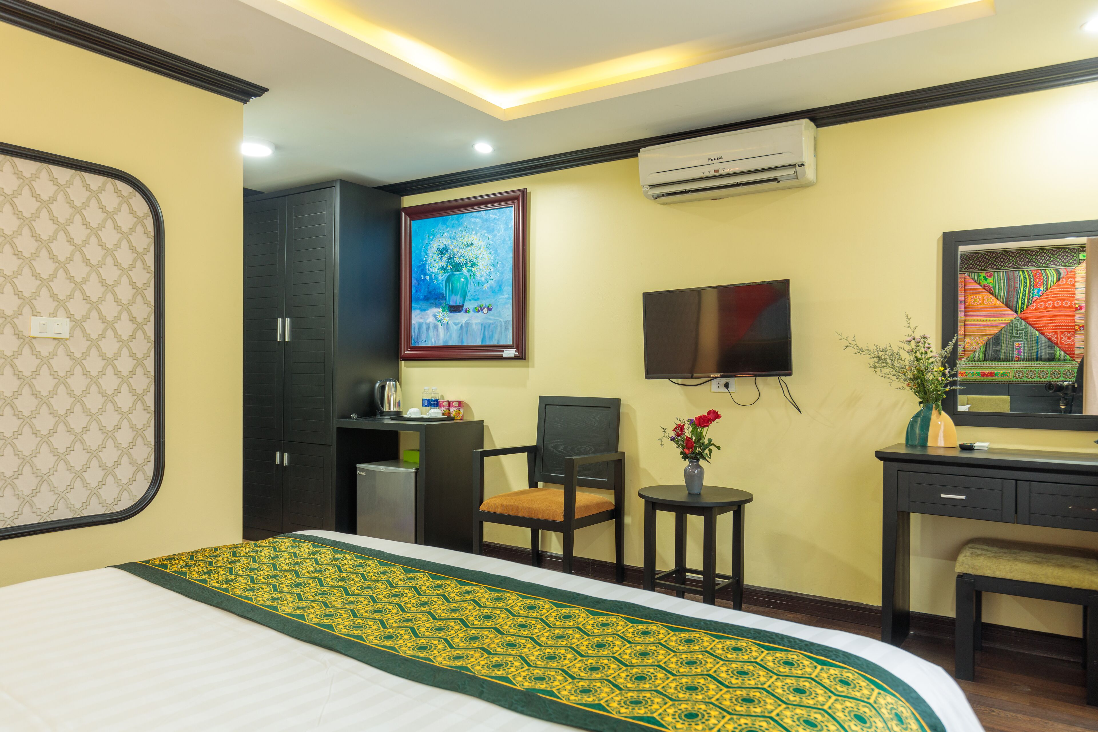A hotel room with a bed, a desk, a chair, a TV, and an air conditioning unit.