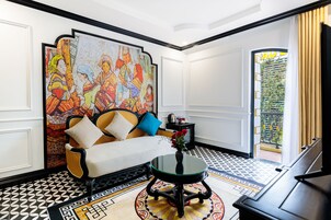 Una habitación con sofá, una mesita con un florero, un mural colorido en la pared y un suelo estampado.