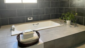 Une salle de bain moderne avec une baignoire, une fenêtre, une plante en pot et un panier rempli de serviettes.