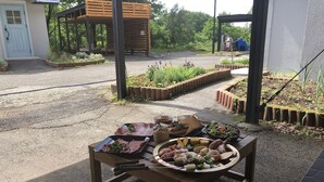 Un espace de restauration en plein air avec une variété de plats disposés sur une table en bois, entouré de parterres de jardin et d’une structure de pergola en bois.