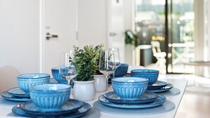 A dining table set with blue glassware and plates, a white vase with a plant, and a city view through a glass door. - The Oasis - Sauna | Parking | Fast WiFi | Airport (Mangere Bridge)
