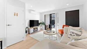 A modern living room with a sofa, a coffee table, and a TV. There is a sliding glass door leading to an outdoor area. - The Oasis - Sauna | Parking | Fast WiFi | Airport (Mangere Bridge)