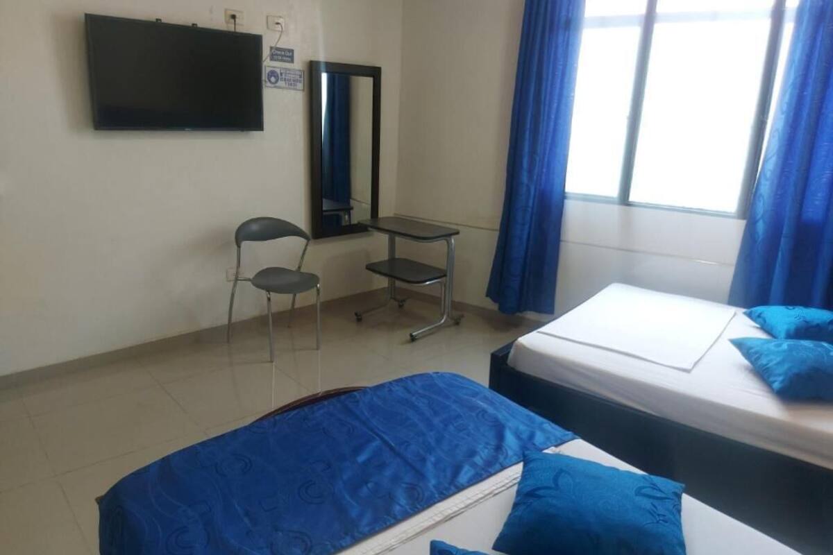 Una habitación con una cama, una silla, una mesita, un televisor y una ventana con cortinas.