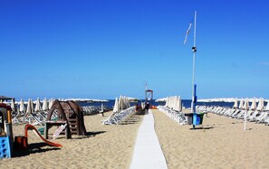 A beach with a white walkway, rows of beach umbrellas, and a lifeguard tower in the distance. - Villa Eusepia, facing the beach of Tirrenia  (Marina di Pisa-tirrenia-calambr)