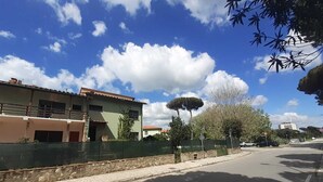 A street with a building that has a green fence, a tree, and a clear blue sky. - Villa Eusepia, facing the beach of Tirrenia  (Marina di Pisa-tirrenia-calambr)