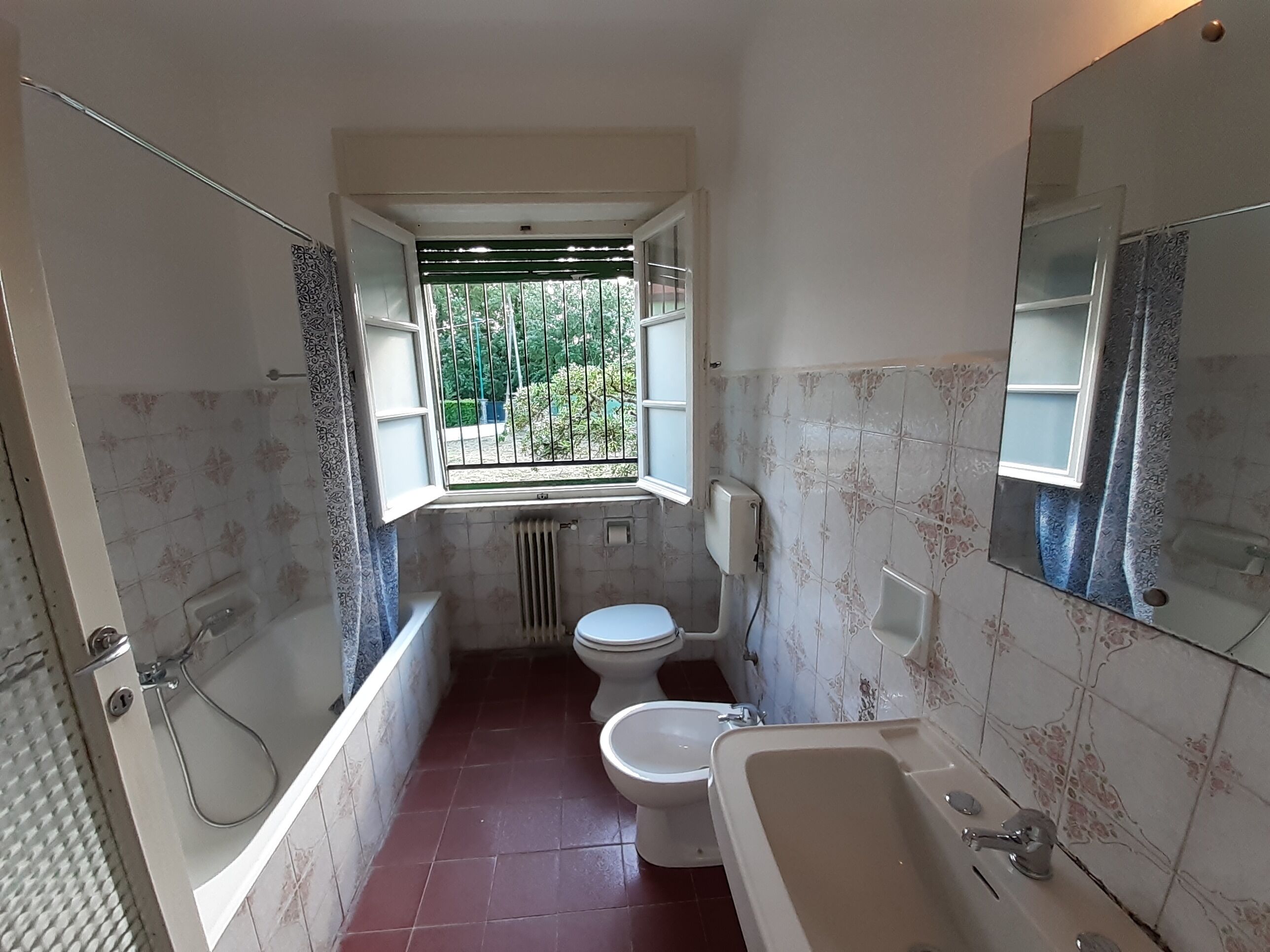 A bathroom with a bathtub, toilet, and a window with a view of greenery.
