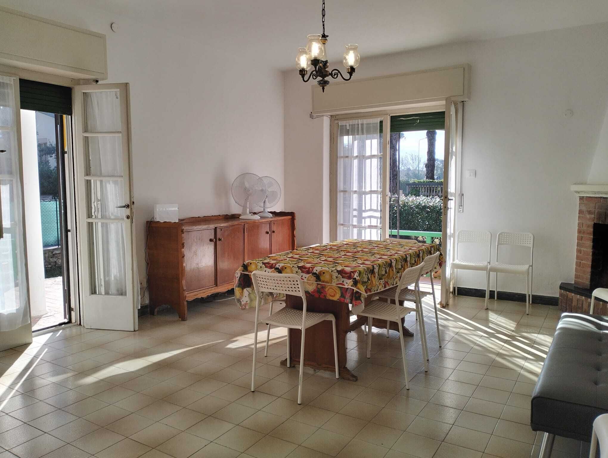 A dining area with a long table, chairs, a wooden cabinet, and a chandelier.