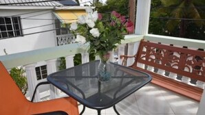 Een balkon met een glazen tafel en oranje stoelen, een vaas met bloemen en uitzicht op een wit gebouw met balkons.
