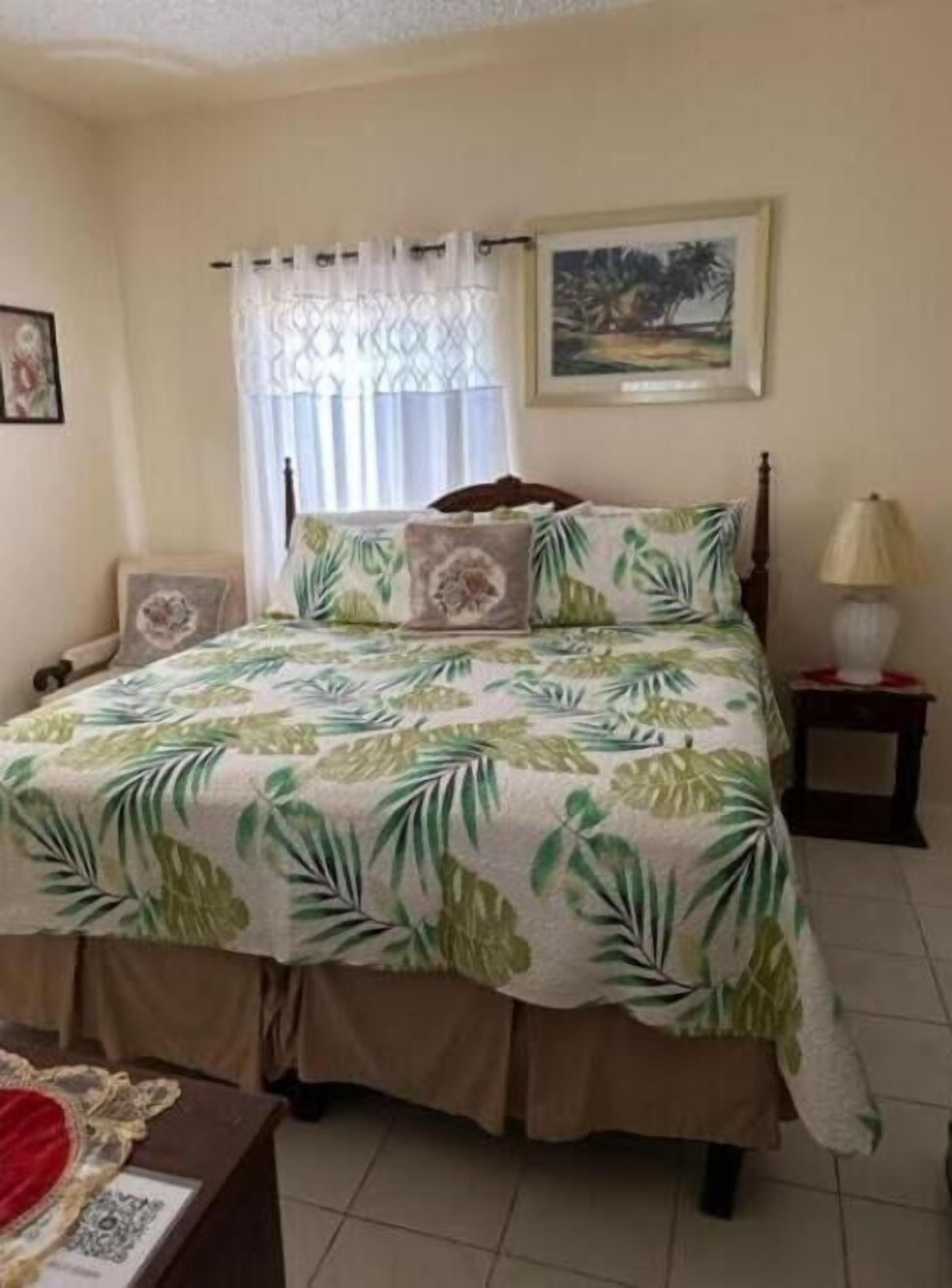 A bedroom with a bed, a nightstand, a lamp, a framed picture on the wall, and a window with curtains.
