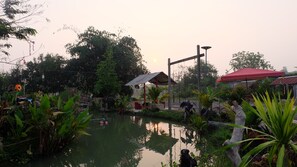 A serene outdoor area with a pond, surrounded by lush greenery and a red-roofed structure.