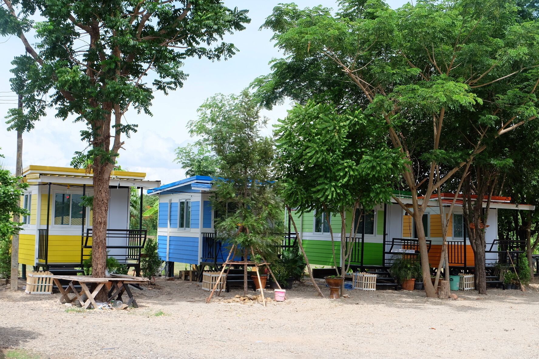A row of colorful cabins with a dirt ground and trees in the background.