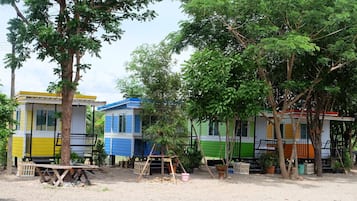A row of colorful cabins with a dirt ground and trees in the background.