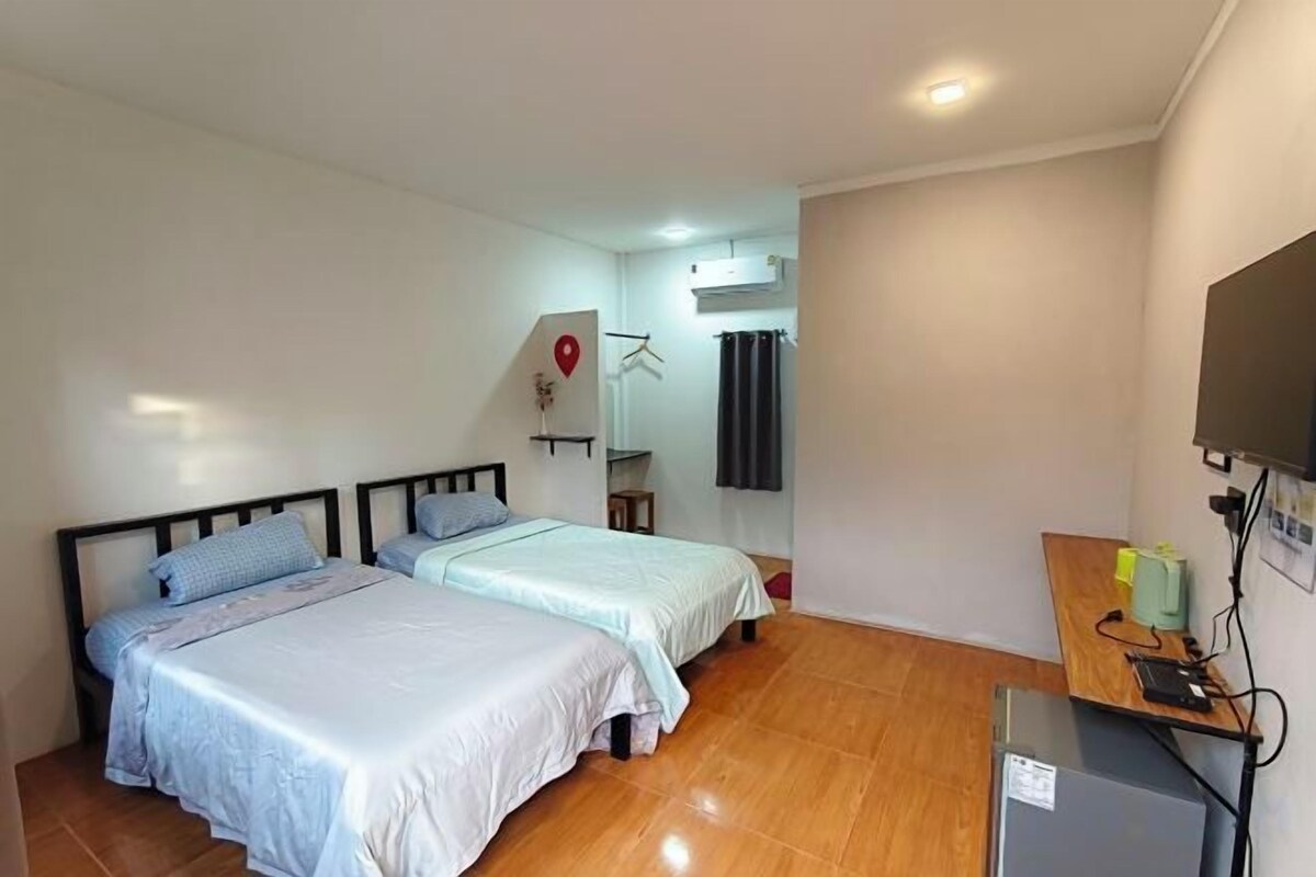 A room with two beds, a desk with a computer, and a small refrigerator.