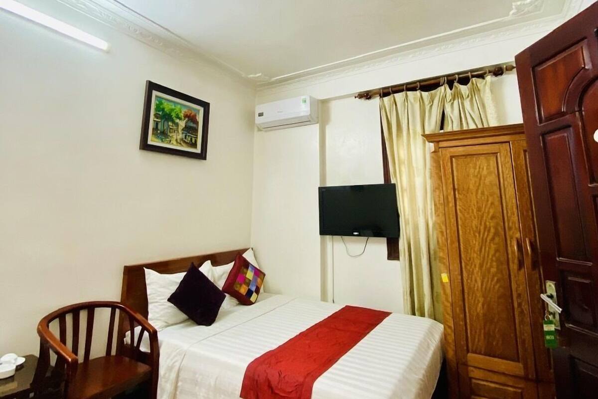 Ein Hotelzimmer mit einem Bett, einem Holzstuhl, einem Fernseher, einer Klimaanlage und einem Kleiderschrank.