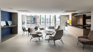 A modern hotel lobby with a reception desk, seating area, and large windows offering views of the city.