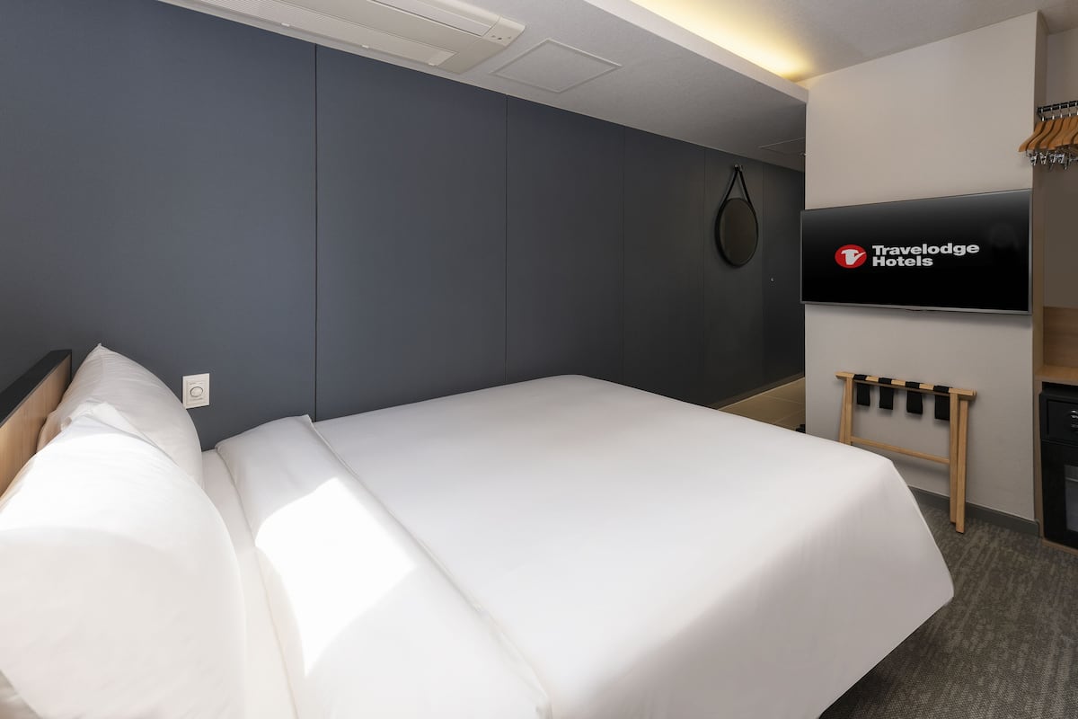 A Travelodge hotel room with a bed, a TV mounted on the wall, and a coat rack.