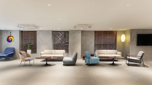 A modern lobby with a seating area featuring sofas and armchairs, a potted plant, and a flat-screen TV mounted on the wall.