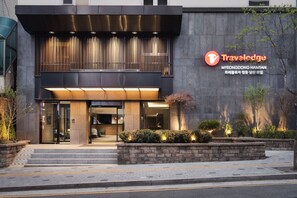 A modern building with a Travelodge sign, featuring a large entrance, steps leading up to the door, and a well-lit facade. - Travelodge Myeongdong Namsan (Seoul)