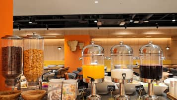 Buffet de café da manhã com diversos dispensadores de alimentos, incluindo cereais, suco de laranja, leite e suco de uva.