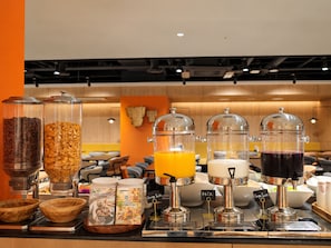 Un bufé de desayuno con varios dispensadores de alimentos, como cereales, jugo de naranja, leche y jugo de uva.