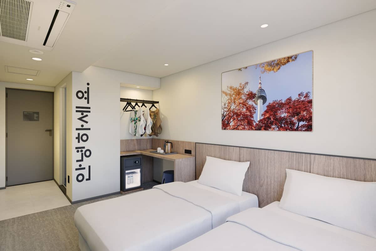 A hotel room with two beds, a small desk, a wardrobe, and a wall-mounted TV.