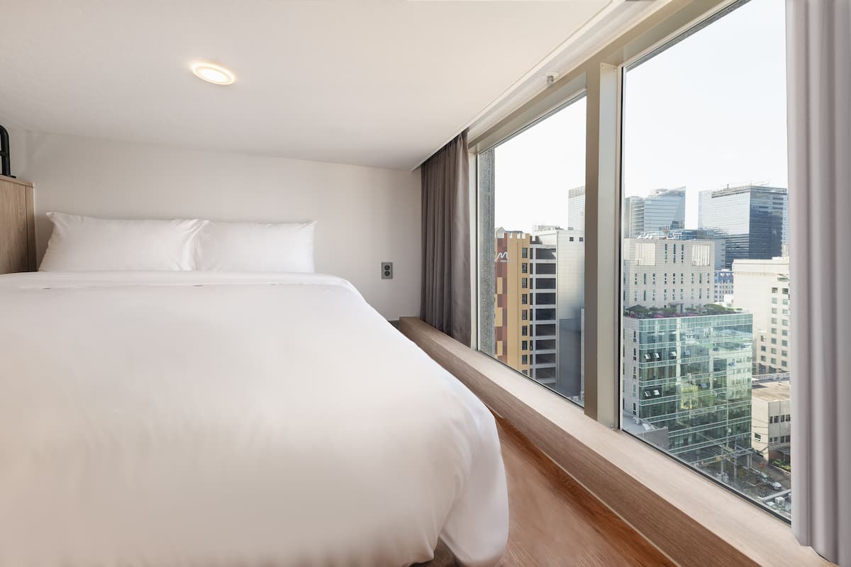 A modern hotel room with a large bed, a window with a city view, and a wooden floor.