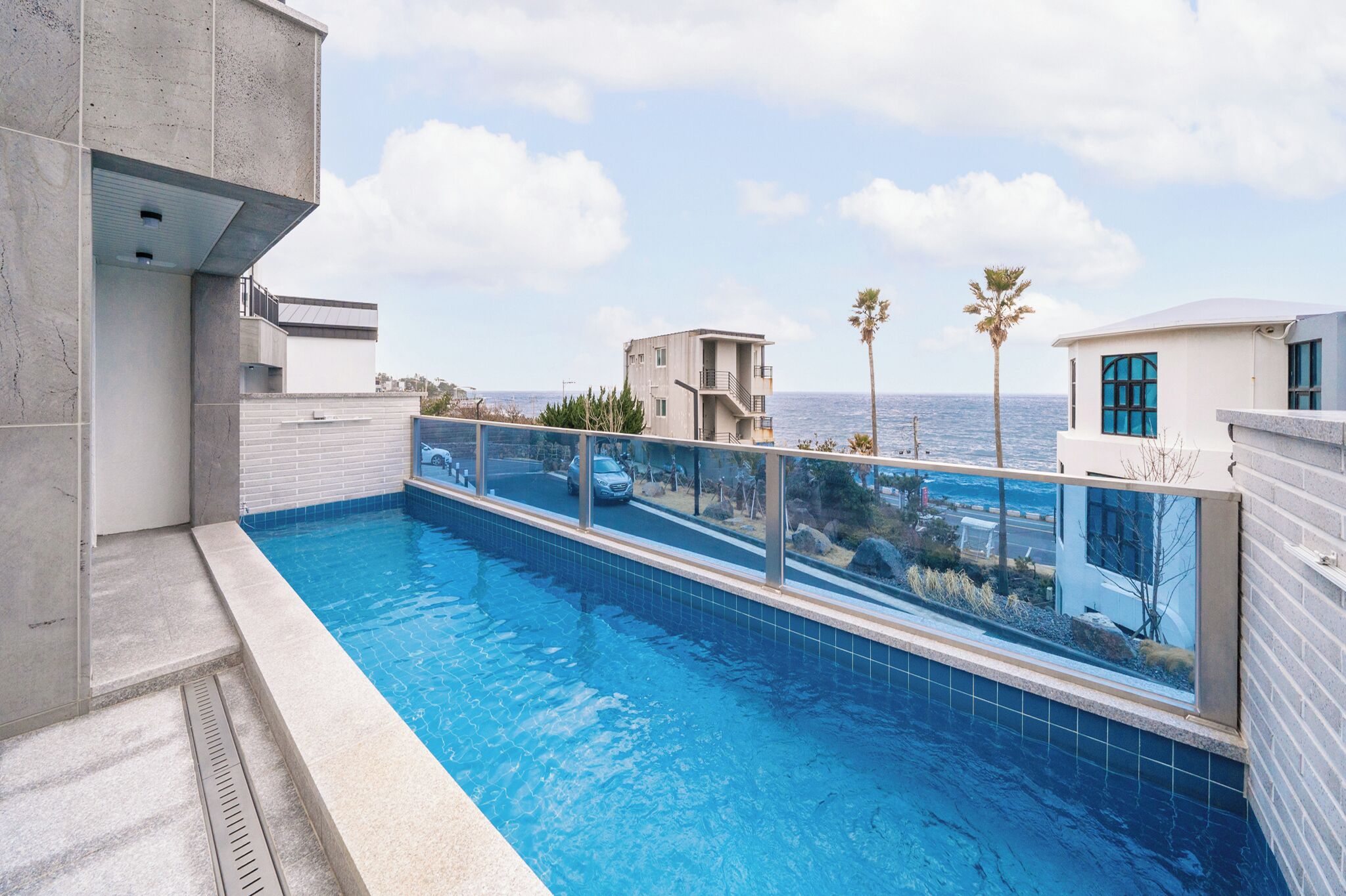 A swimming pool with a view of the sea, a modern building, and a palm tree.