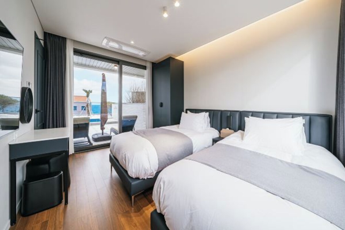 Habitación de hotel moderna con dos camas, un escritorio y un ventanal con vistas al exterior.