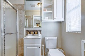 A bathroom with a shower, toilet, sink, and a mirror.
