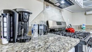 A kitchen with a gas stove, coffee maker, and water bottles on the counter.
