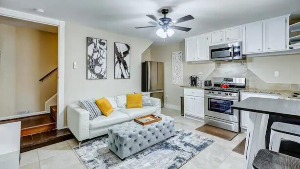 A modern kitchen with white cabinets, a microwave, stove, and a ceiling fan.