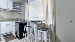 A compact kitchen with white cabinets, a black countertop, and a small dining area with two stools.