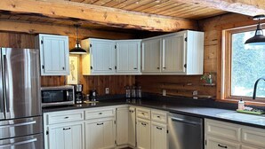 A modern kitchen with white cabinets, stainless steel appliances, and a wooden ceiling. - Log Cabin with Mountains and Lake View, enjoy relaxing in the hot tub (Clam Gulch)