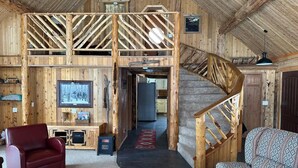 A rustic wooden interior with a high ceiling, a staircase, a red leather chair, a patterned sofa, and a television. - Log Cabin with Mountains and Lake View, enjoy relaxing in the hot tub (Clam Gulch)