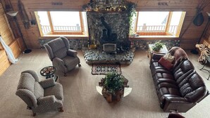 A cozy cabin interior with a stone fireplace, leather sofas, and a high ceiling with wooden beams. - Log Cabin with Mountains and Lake View, enjoy relaxing in the hot tub (Clam Gulch)