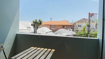 A balcony with a wooden table and chairs, a potted plant, and a view of buildings and a clear sky.